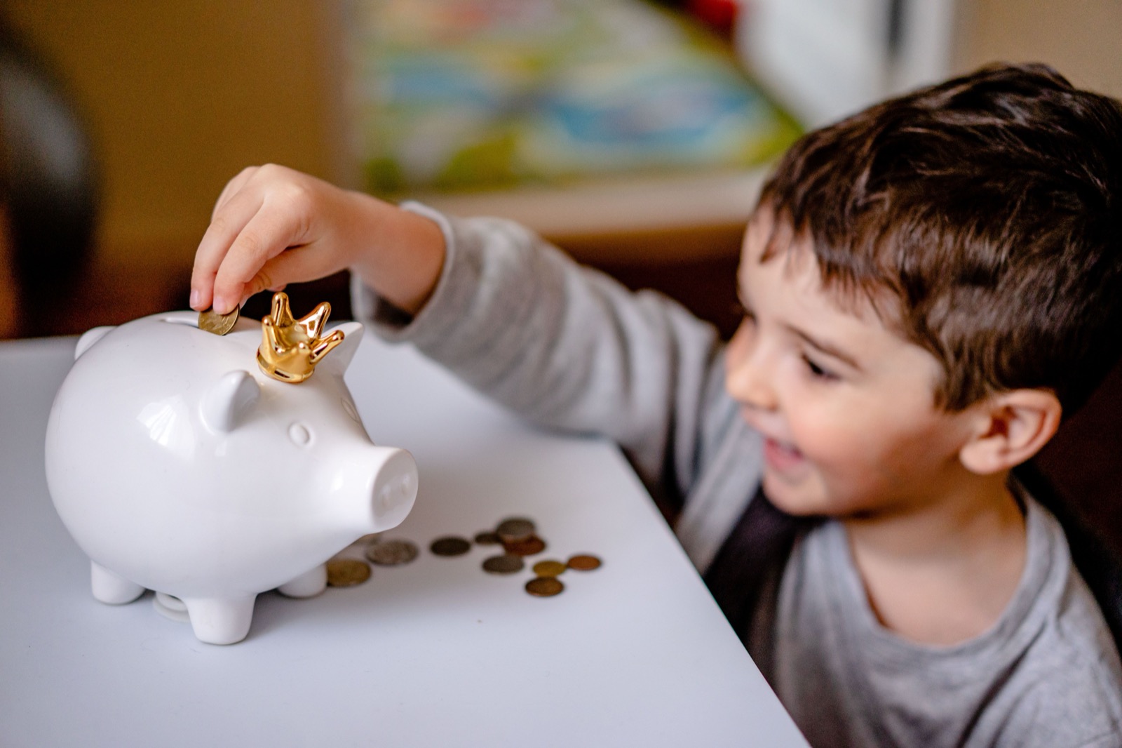 A child placing a coin into a white piggy bank at a table.