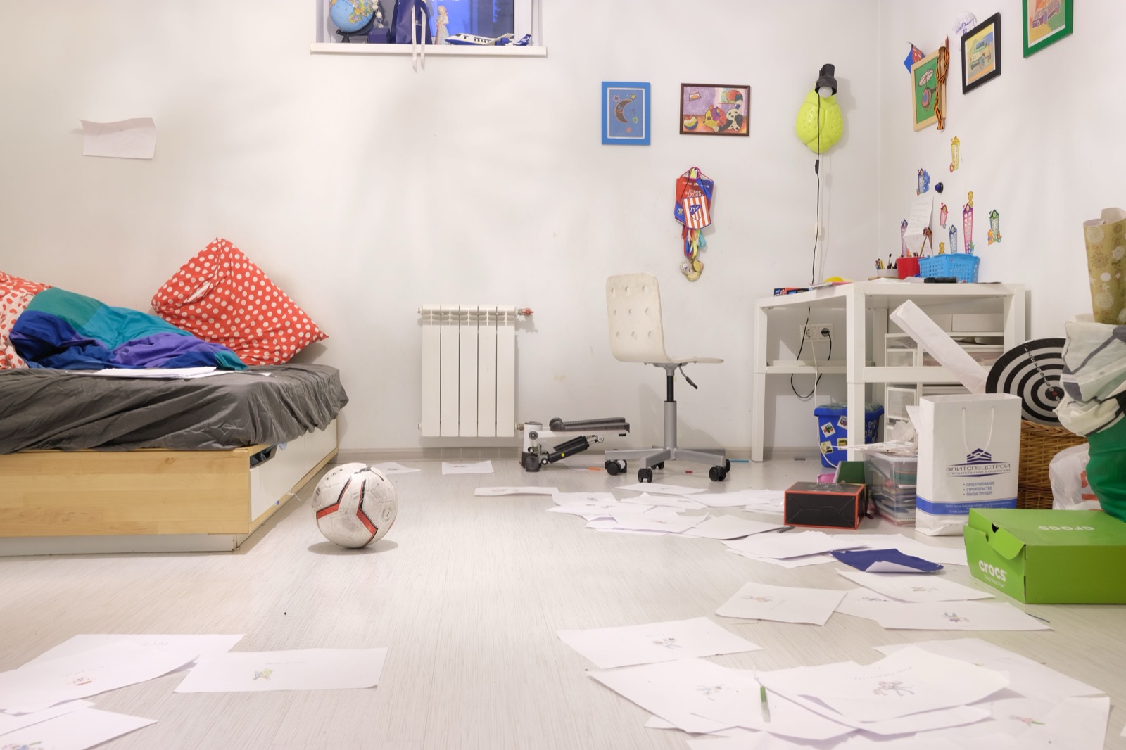 A child's bedroom with papers and toys scattered across the floor.