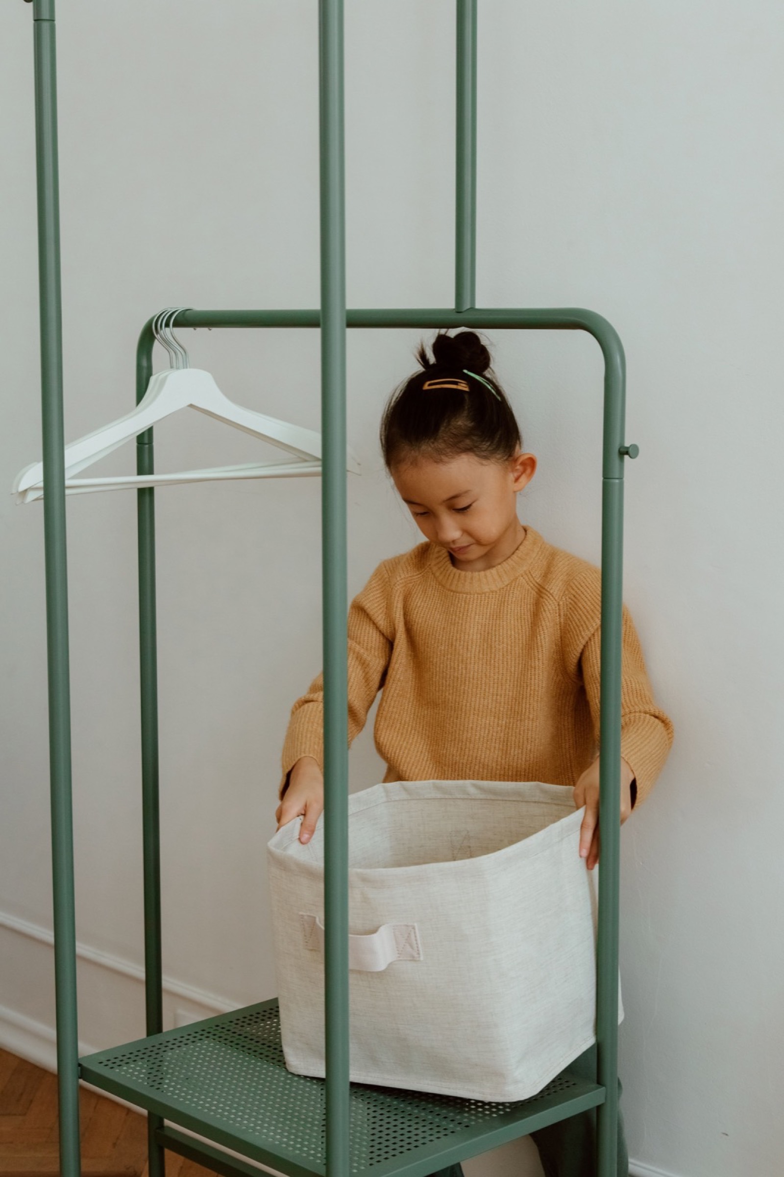 A young child putting a storage bin onto a green rack at home.